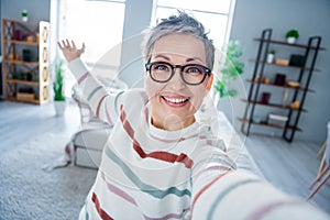 Photo of friendly positive grandmother toothy smile take selfie arm demonstrate modern house indoors