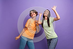 Photo of funky carefree girls dressed t-shirts smiling dancing having fun isolated purple color background