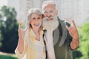 Photo of funky cool senior couple wear casual clothes walking showing hard rock sign smiling outside urban city street