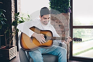 Photo of funky cool young guy wear white shirt singing song playing guitar indoors apartment room
