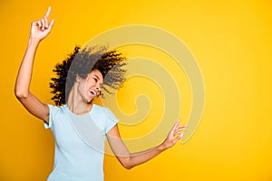 Photo of funky cute dark skin curly girl dressed blue t-shirt dancing pointing empty space isolated yellow color