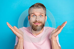 Photo of funky doubtful young guy dressed pink t-shirt rising arms shrugging shoulders isolated blue color background