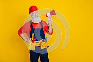 Photo of funky excited age man wear overall uniform red hard hat talking loud speaker empty space isolated yellow color