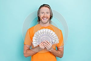 Photo of funky excited guy dressed orange t-shirt rising money fan smiling isolated teal color background