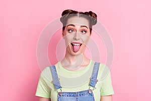 Photo of funky foolish girl grimace crossed eyes protrude tongue wear jeans overall green t-shirt isolated on pink photo