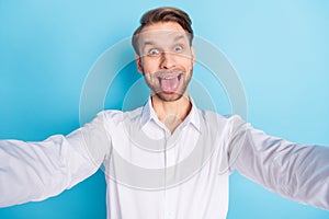 Photo of funky happy crazy young man take selfie make funny face fooling isolated on blue color background