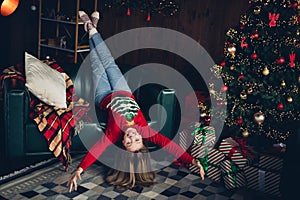 Photo of funky nice positive schoolgirl with blond hair wear red sweater lay upsaide down on couch near christmas tree