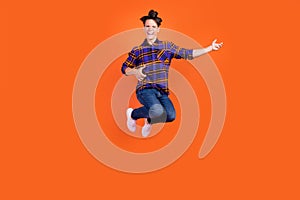 Photo of funky pretty teen boy wear plaid outfit spectacles smiling jumping high playing guitar isolated orange color