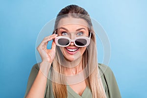 Photo of funky shocked young lady wear green outfit arm dark spectacles smiling isolated blue color background