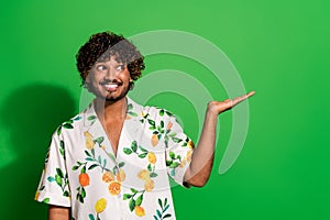 Photo of funky tricky arabian man wear print shirt looking holding arm empty space isolated green color background