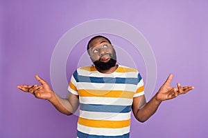 Photo of funky unsure man wear striped t-shirt shrugging shoulders looking empty space isolated violet color background