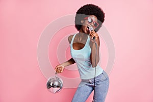 Photo of funky young dark skin woman wear jeans hold disco ball mic singer isolated on pink color background