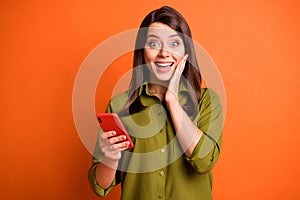 Photo of funny amazed lady hold telephone palm cheekbone wear green shirt isolated orange color background photo
