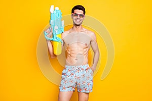 Photo of funny brunet young guy hold gun wear eyewear shorts isolated on yellow color background