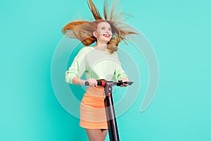 Photo of funny carefree young woman wear green shirt riding scooter looking empty space isolated teal color background