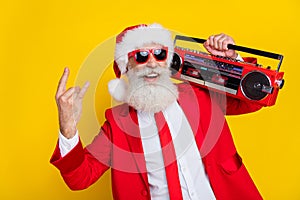 Photo of funny charming claus wear red tux costume tux showing hard rock gesture listening boom box isolated yellow
