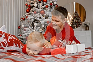 Photo of funny cheerful father tickle his laughing little son wearing red sweaters in decorated xmas room