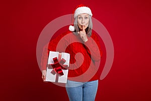 Photo of funny cute secretive granny hold giftbox make shh sign wear hat pullover isolated red color background