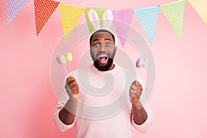 Photo of funny dark skin guy visit family easter party hold festive colorful painted eggs on sticks wear sweater pants