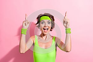 Photo of funny excited lady dressed green sportive bodysuit pointing two fingers up empty space isolated pink color