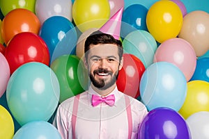 Photo of funny gentleman guy surrounded colorful balloons arranging birthday party wear paper cone cap pink shirt bow