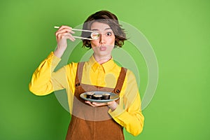 Photo of funny girl hold chopsticks plate sushi hide eye with roll pout lips wear yellow shirt overall isolated green