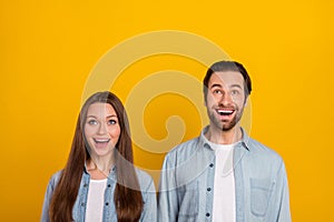 Photo of funny impressed husband wife wear jeans shirts looking up empty space isolated yellow color background