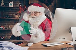 Photo of funny jolly holly santa claus x-mas christmas worker sit table open envelope read wish list letter in house