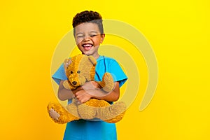 Photo of funny little child with curly hair dressed blue stylish t-shirt hold bear toy laugh  on vibrant yellow