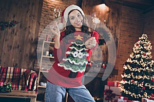 Photo of funny millennial brunette lady hold champagne sparklers wear holliday sweater hat at home alone