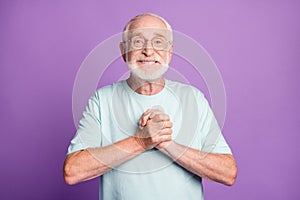 Photo of funny old beard man putting hands together wear light blue t-shirt isolated on purple color background