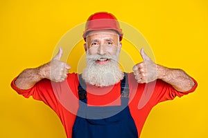 Photo of funny pretty senior guy dressed uniform overall red hardhat showing two thumbs up isolated yellow color