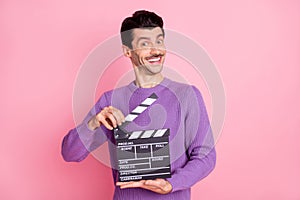 Photo of funny sweet young man dressed purple pullover holding clapperboard isolated pink color background