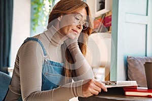 Photo of ginger mature woman reading magazine while sitting at table