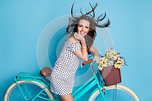 Photo of girl bicycle flowerpot wind blow hair hand face white smile wear dotted short dress isolated blue color