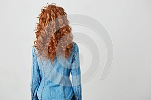 Photo of girl with red curly hair standing back to camera over white background. Copy space.