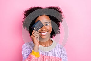 Photo of girlish satisfied optimistic girl with perming coiffure wear knit sweater eye cover debit card isolated on pink