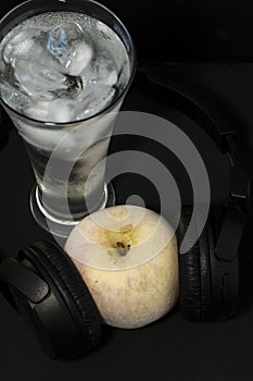 Photo of a glass with ice and frozen apple in headphones close-up on a black background