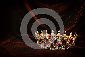 photo of gold crown over gothic dark silk background. Medieval period concept.