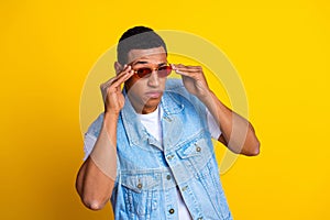 Photo of good mood cool handsome man dressed denim vest over t-shirt touch sunglass posing on camera isolated on yellow