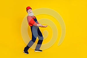 Photo of good mood funky senior guy dressed uniform overall red hardhat holding arms heave empty space isolated yellow