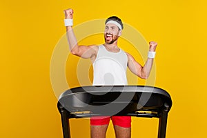 Photo of good mood lucky guy activewear walking treadmill rising fists empty space isolated yellow color background