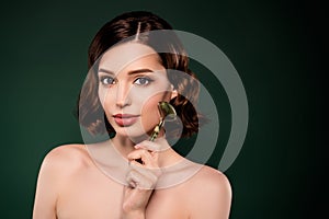 Photo of good mood smiling female using mezoroller on face lifting spa procedure isolated on green color background