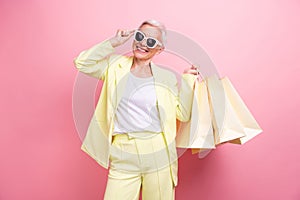 Photo of gorgeous business lady mature age in yellow suit bring packages shopping bags touching sunglass isolated on