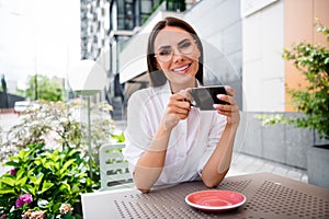 Photo of gorgeous peaceful girl toothy smile hands hold aroma coffee mug enjoy lunch break cafe outside