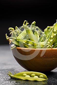 Photo of green pea pods in wooden plate on empty black table with pod