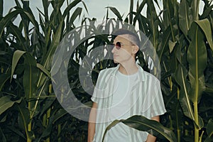 Photo of a guy in fashionable sunglasses. A man in a corn field with leaves. Evening photo with flash