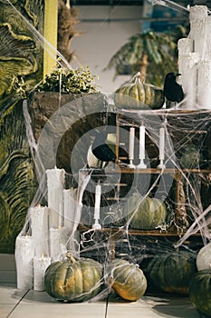 Photo of Halloween decorations with crows, pumpkins, candles and shelves indoors. Vertical