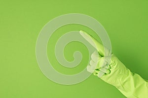 Photo of hand in green rubber glove making pointing symbol with forefinger on isolated green background with copyspace