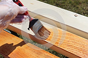 Photo of a hand painting a wooden beam with brown glazing varnish. Brush in the hands of the painter.